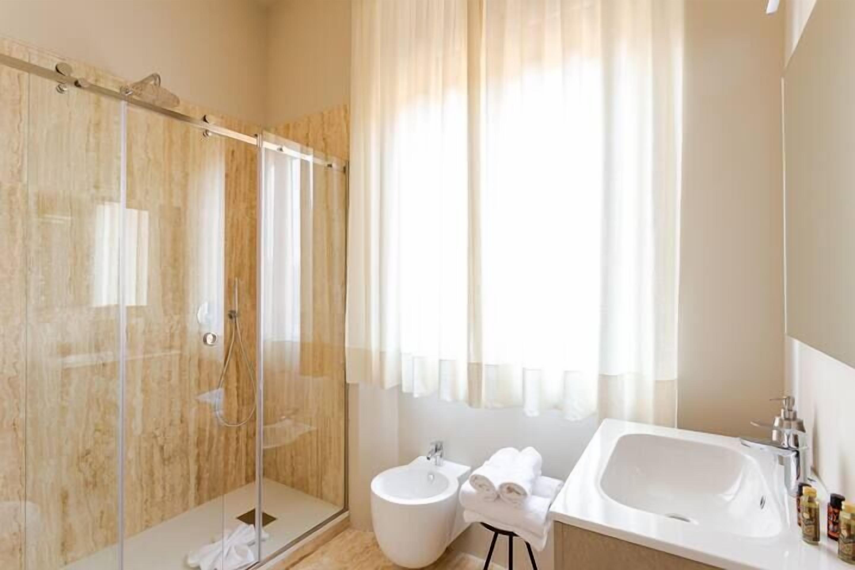 A modern bathroom with a glass-enclosed shower, a standalone bidet, and a large bathtub.