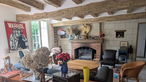 A cozy living room with a fireplace, wooden beams, a coffee table, and a variety of decorative items.