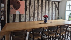 A dining area with a wooden table and chairs, a vase with red flowers, and a textured wall with vertical wooden beams.