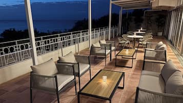 An outdoor patio with wicker furniture, a wooden table, and a view of the ocean at dusk.