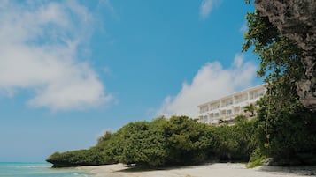 A beachfront hotel with a white exterior, lush greenery, and a clear blue sky.