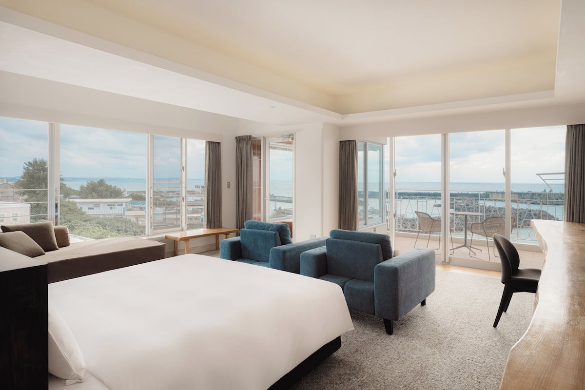A hotel room with a large bed, seating area, and a balcony with a view.