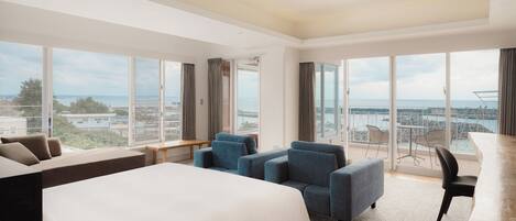 Habitación de hotel con cama grande, zona de estar y balcón con vistas.