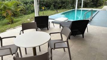 Een zwembadgedeelte met een ronde tafel en stoelen, omgeven door een weelderige tuin en een helder zwembad.