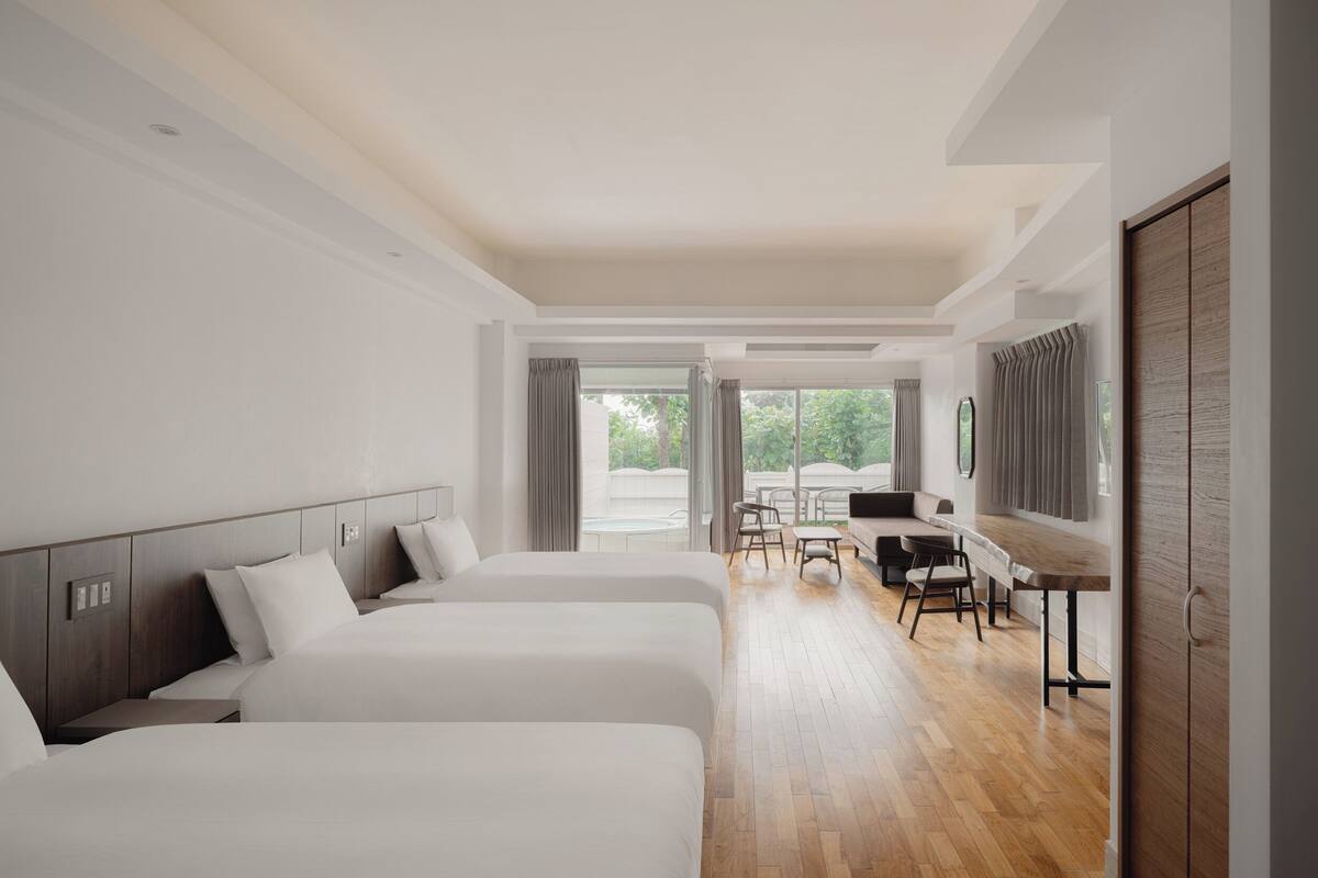 A hotel room with two beds, a desk, and a view of the outdoors.