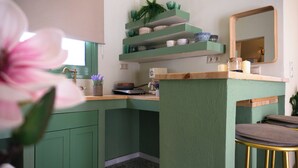 Eine Küche mit grünen Schränken, einer Holz Arbeitsplatte, einem Spülbecken mit Messingarmatur und einem Spiegel über der Arbeitsplatte.