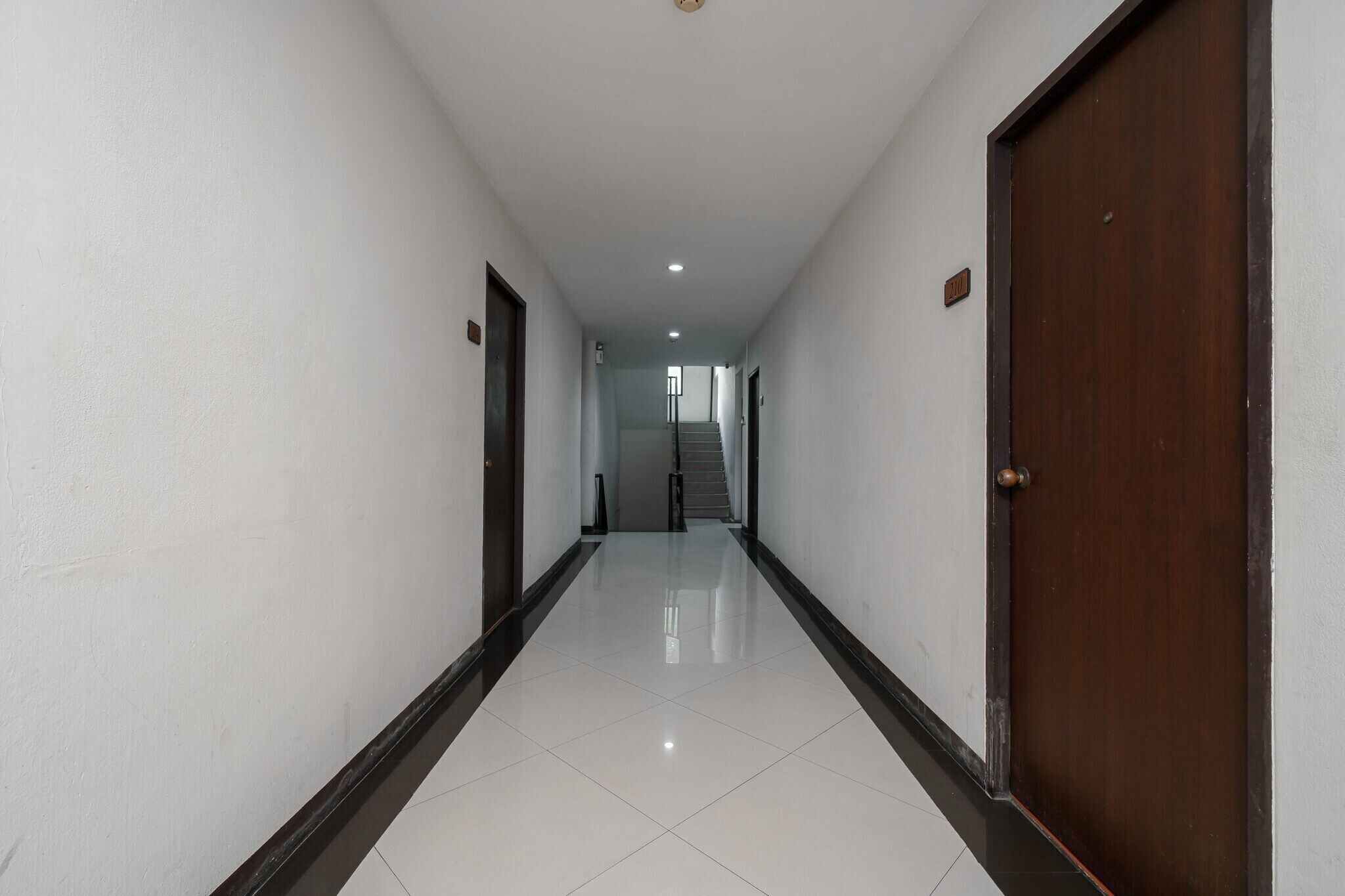 A hallway with white walls and a shiny tiled floor, leading to a staircase.
