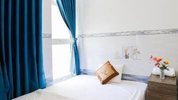 A bedroom with a bed, blue curtains, a wooden dresser, and a small table with a vase of flowers.