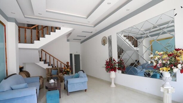A modern living room with a staircase, blue sofas, a coffee table, and a large mirror reflecting the room. - Tram Anh Hotel Dong Nai - by BAY LUXURY (Nhon Trach)