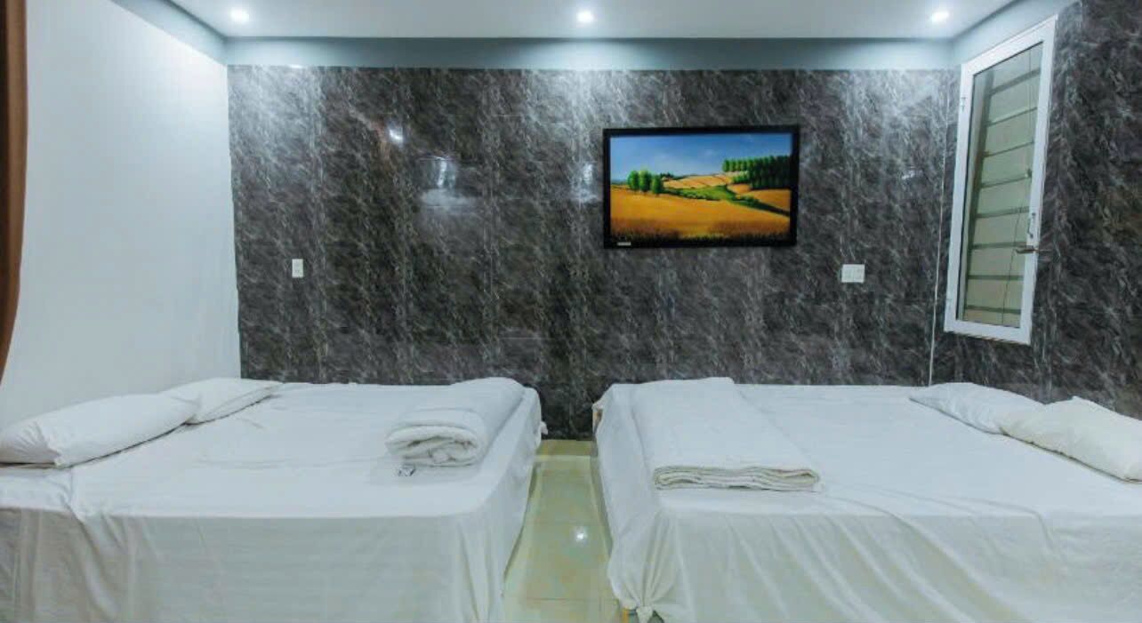 A hotel room with two beds, a TV mounted on the wall, and a window with a view of a landscape.