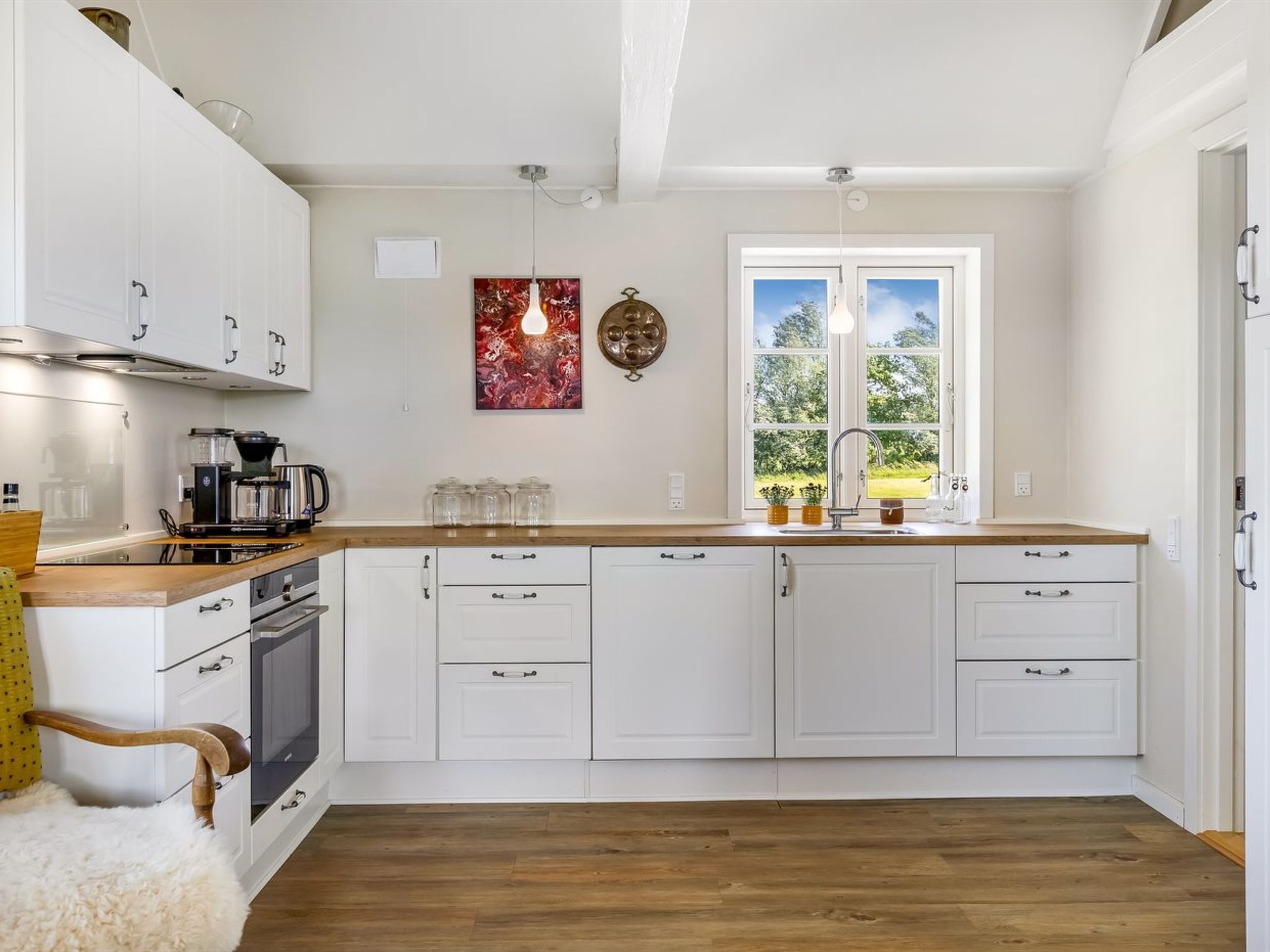 A modern kitchen with white cabinetry, a wooden countertop, a built-in oven, and a window with a view of greenery.