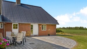 A brick house with a tiled roof and a paved patio area with outdoor furniture.