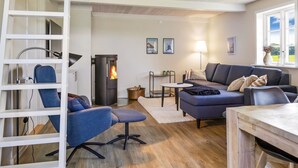 A cozy living room with a modern fireplace, a blue sofa, a wooden dining table, and a white ladder.