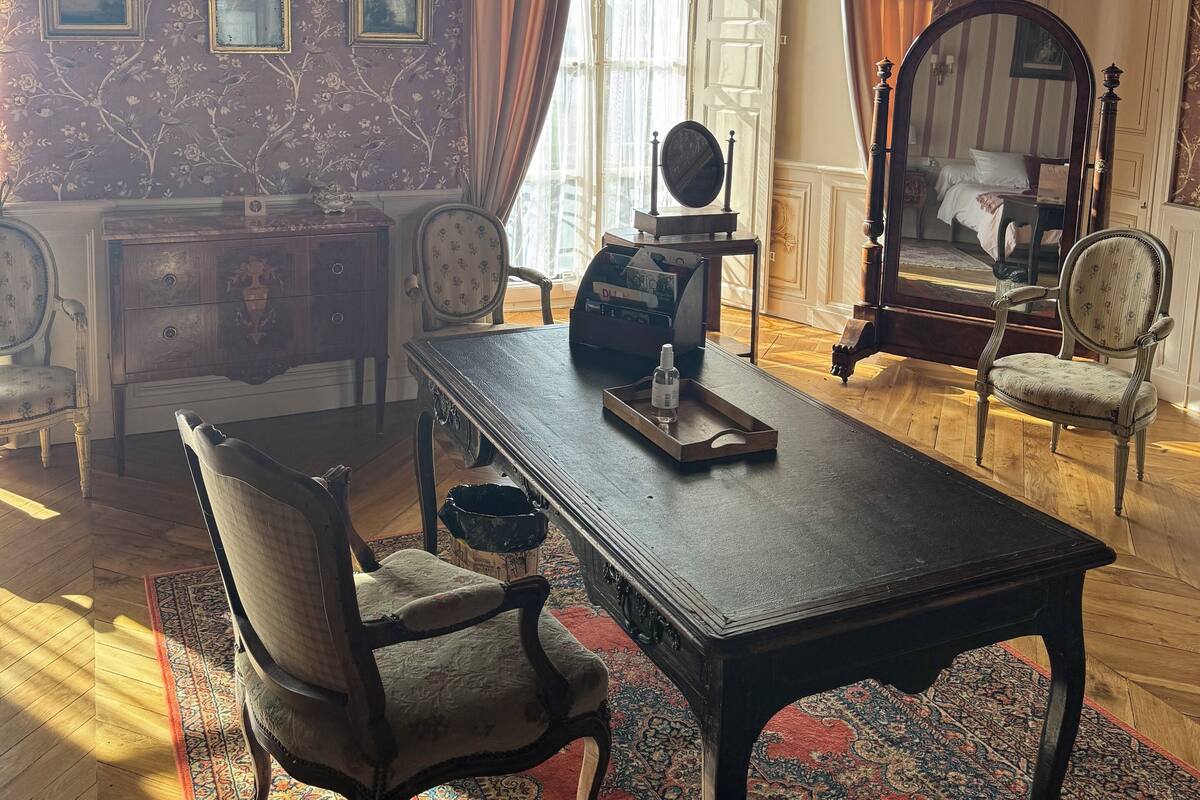 Quarto com mesa de madeira, duas cadeiras, penteadeira e espelho.