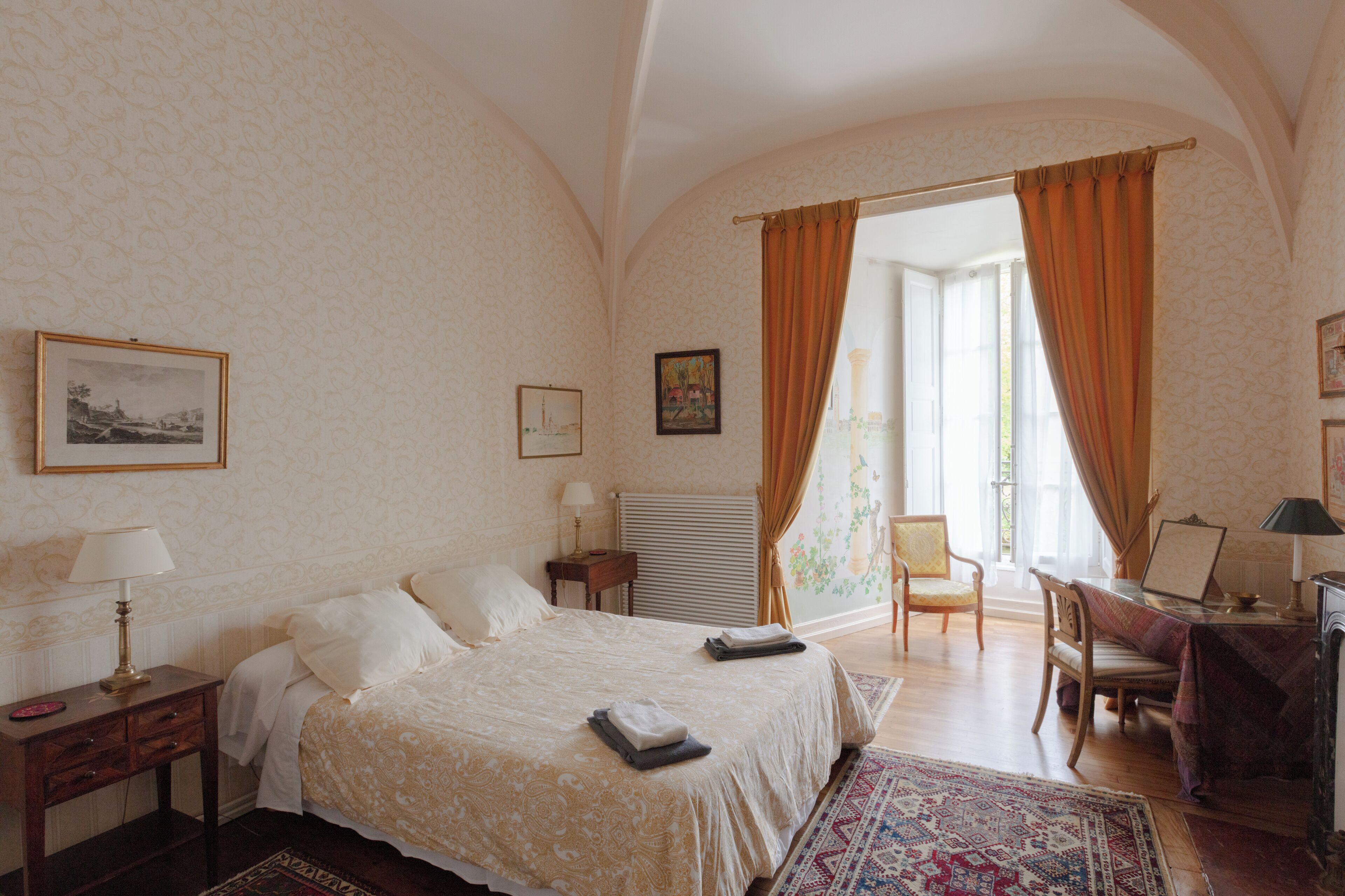 A bedroom with a large bed, a desk, a chair, and a window with curtains.