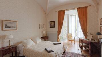 A bedroom with a large bed, a desk, a chair, and a window with curtains.
