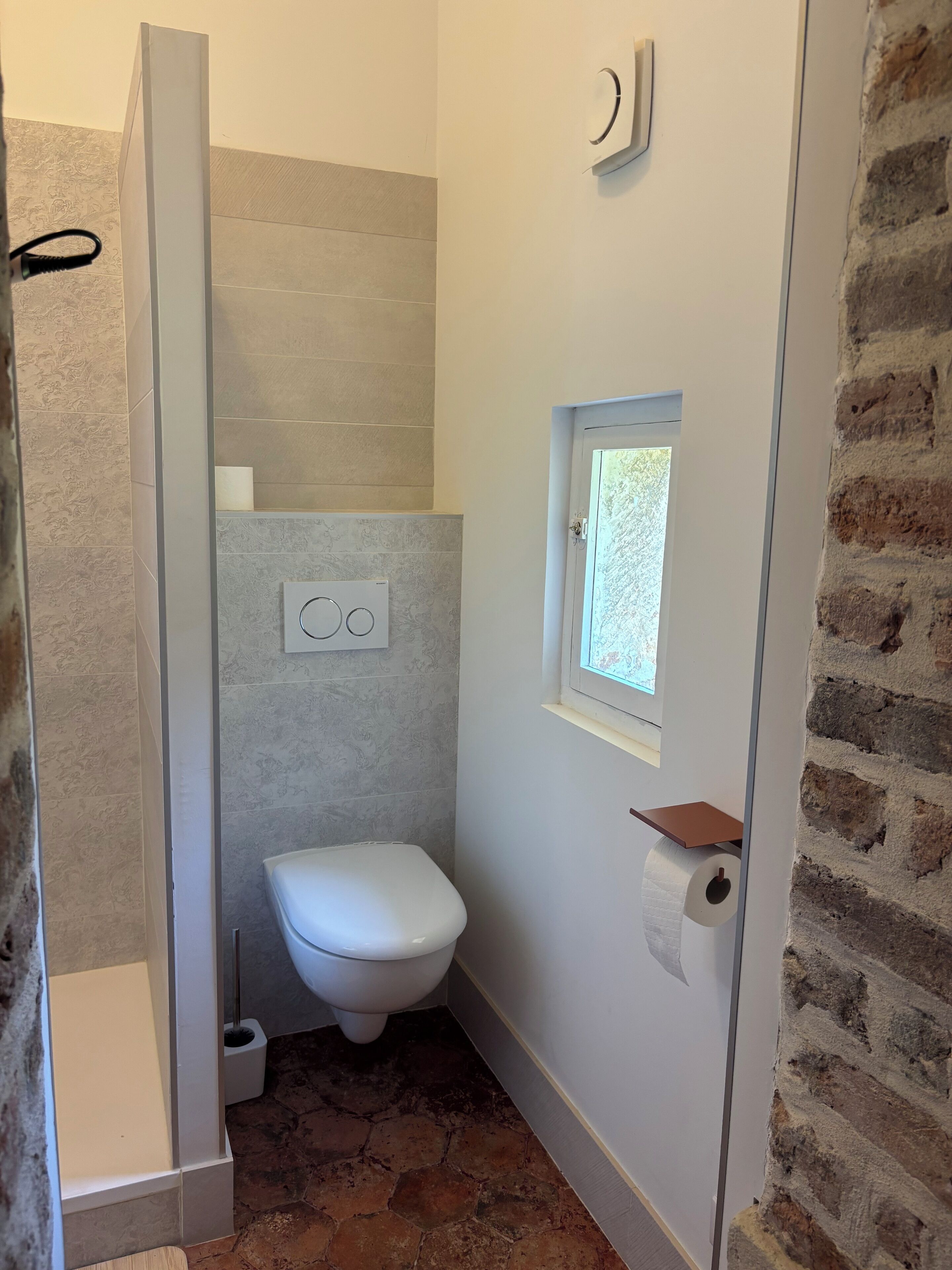 Une petite salle de bain comprenant des toilettes, un espace douche et une petite fenêtre.