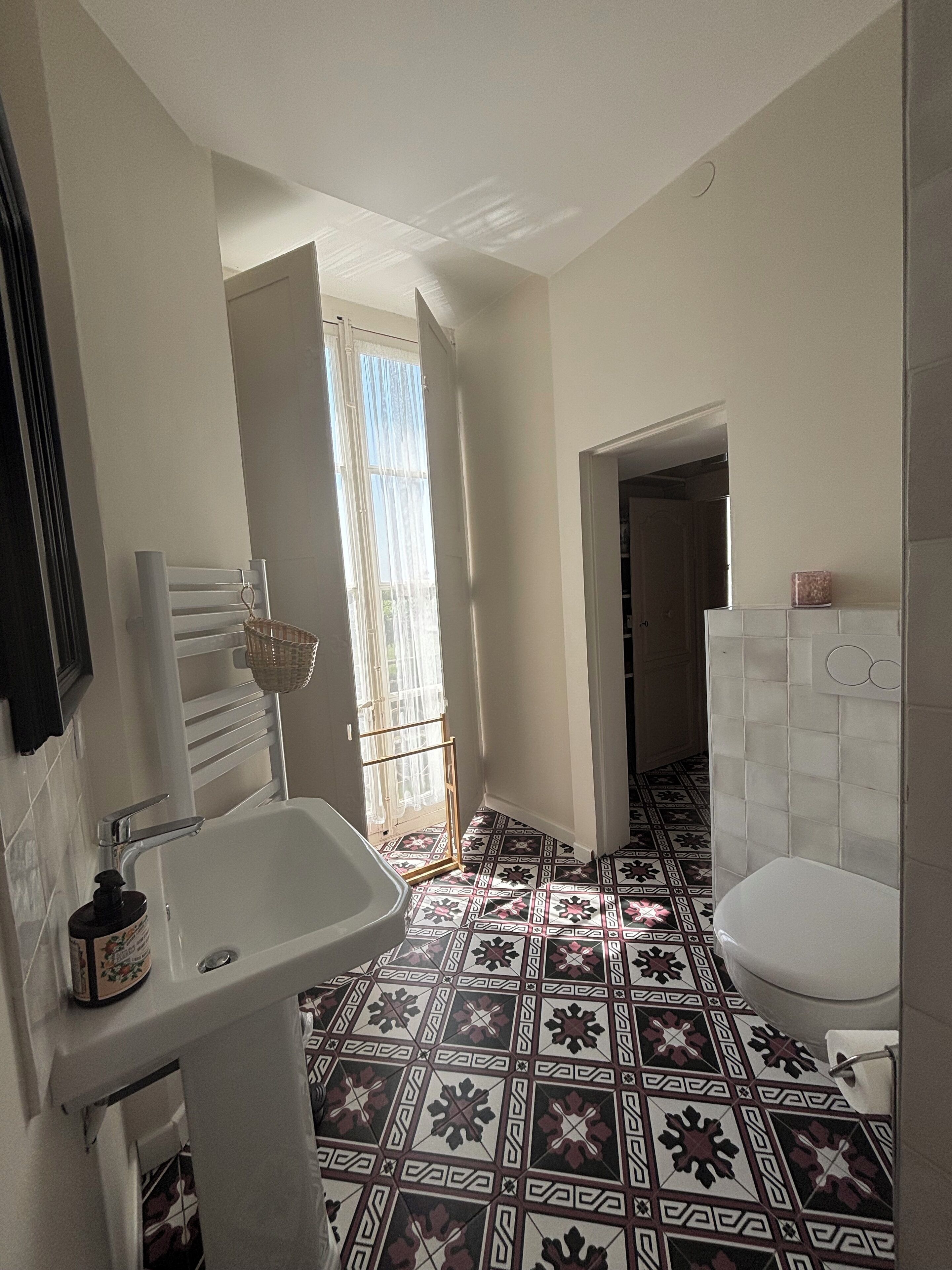 Casa de banho com lavatório branco, sanita e ladrilhos com padrão.