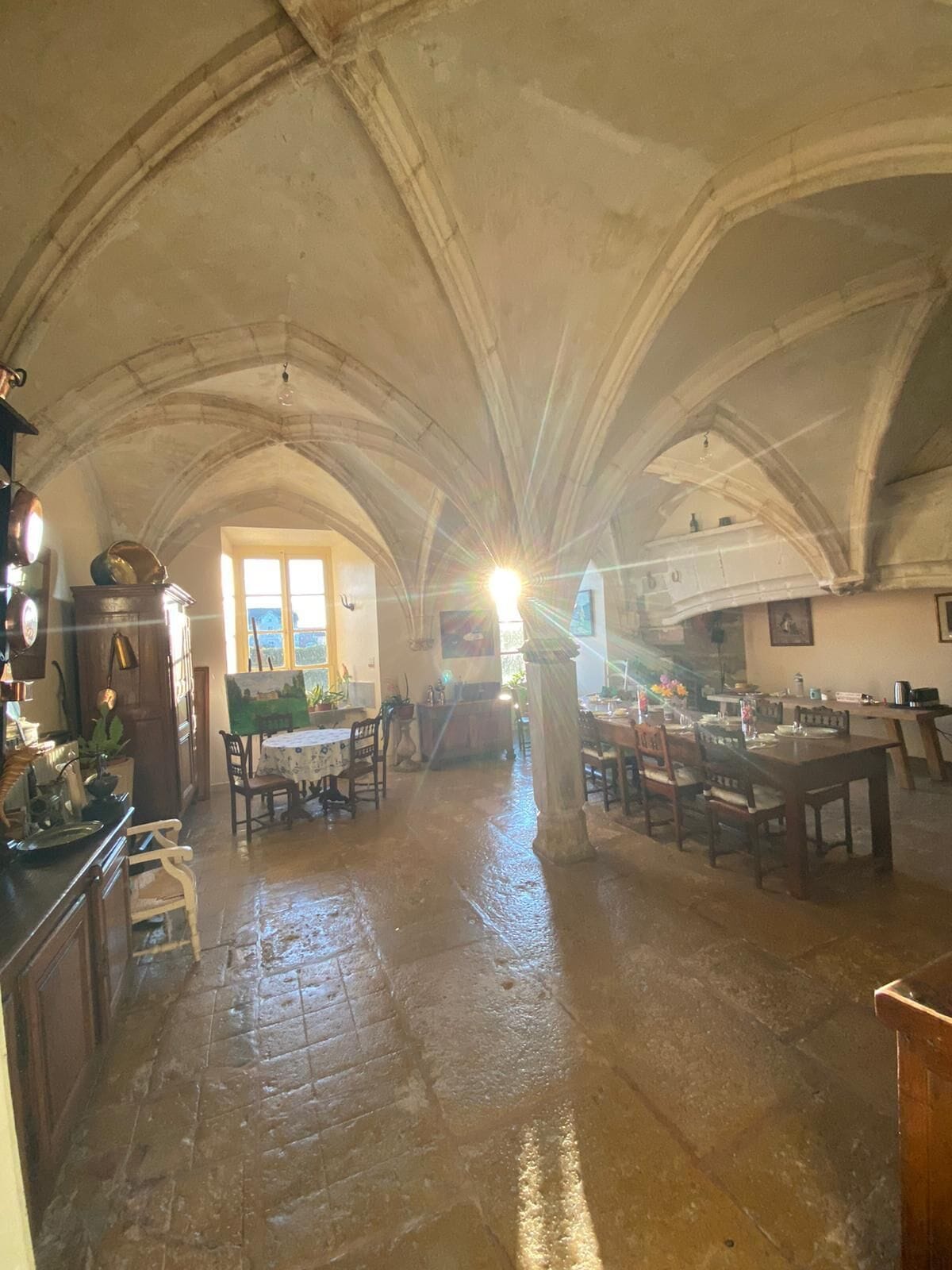 A spacious kitchen with high ceilings and arched stonework, featuring a central island, dining area, and a view through a doorway.
