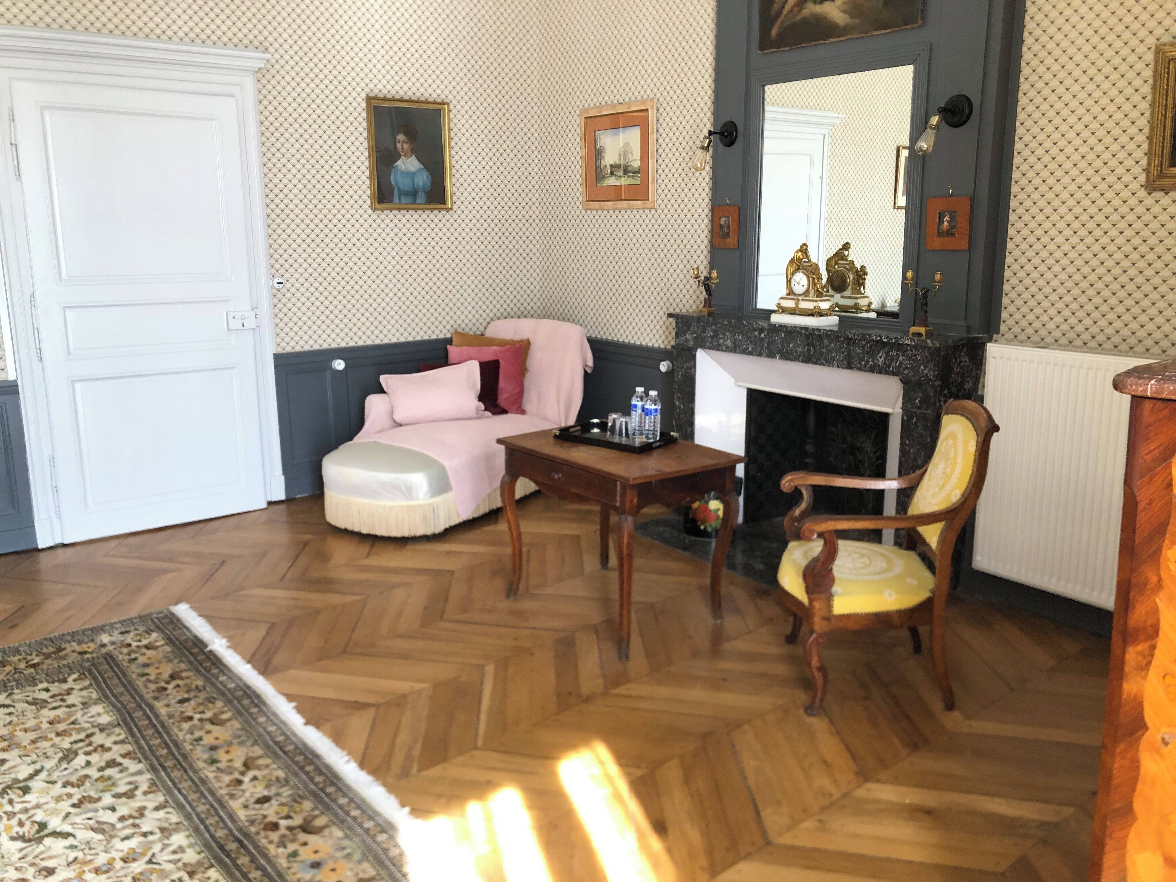 A living room with a sofa, armchair, and a fireplace. There is a door and a patterned wall.