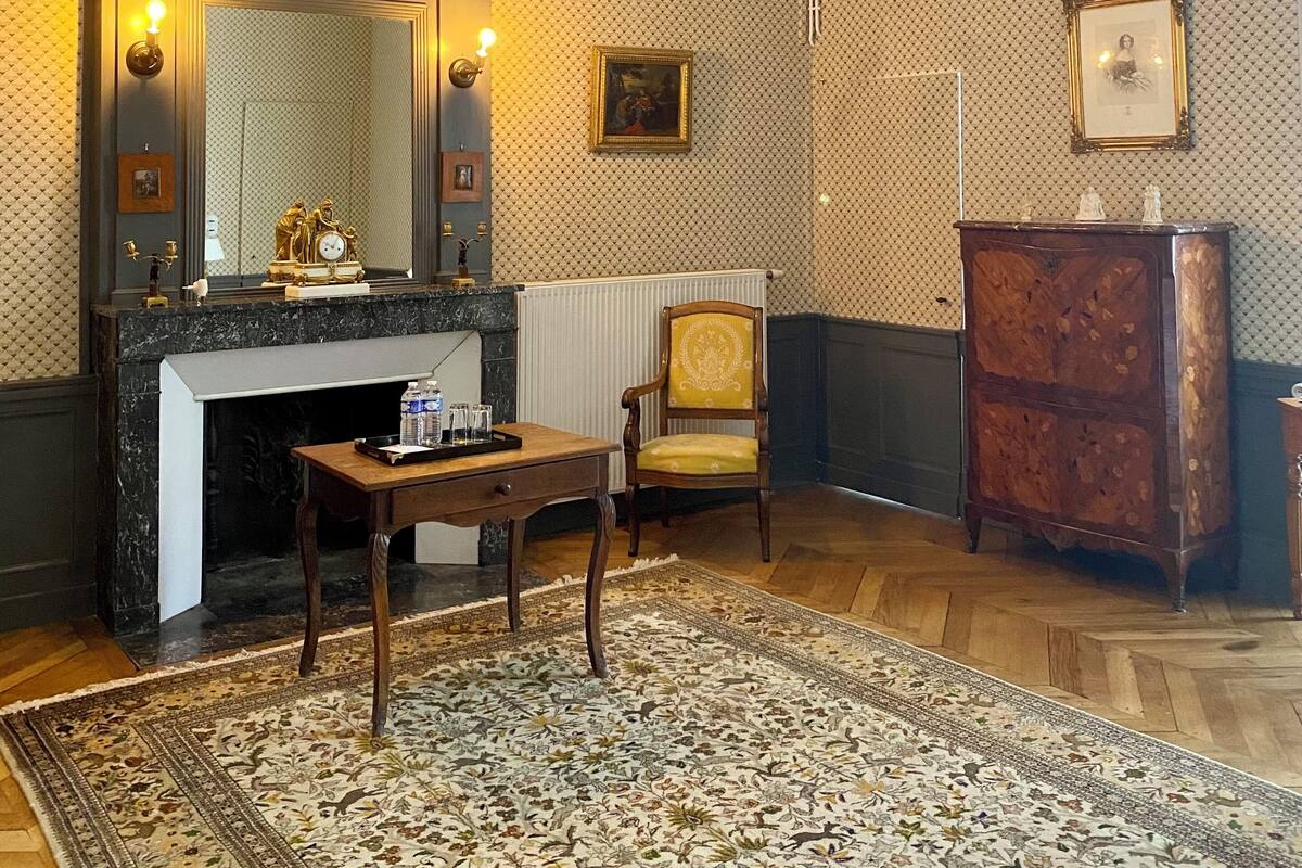 Quarto com lareira, uma cadeira de madeira, mesa, espelho e tapete estampado.