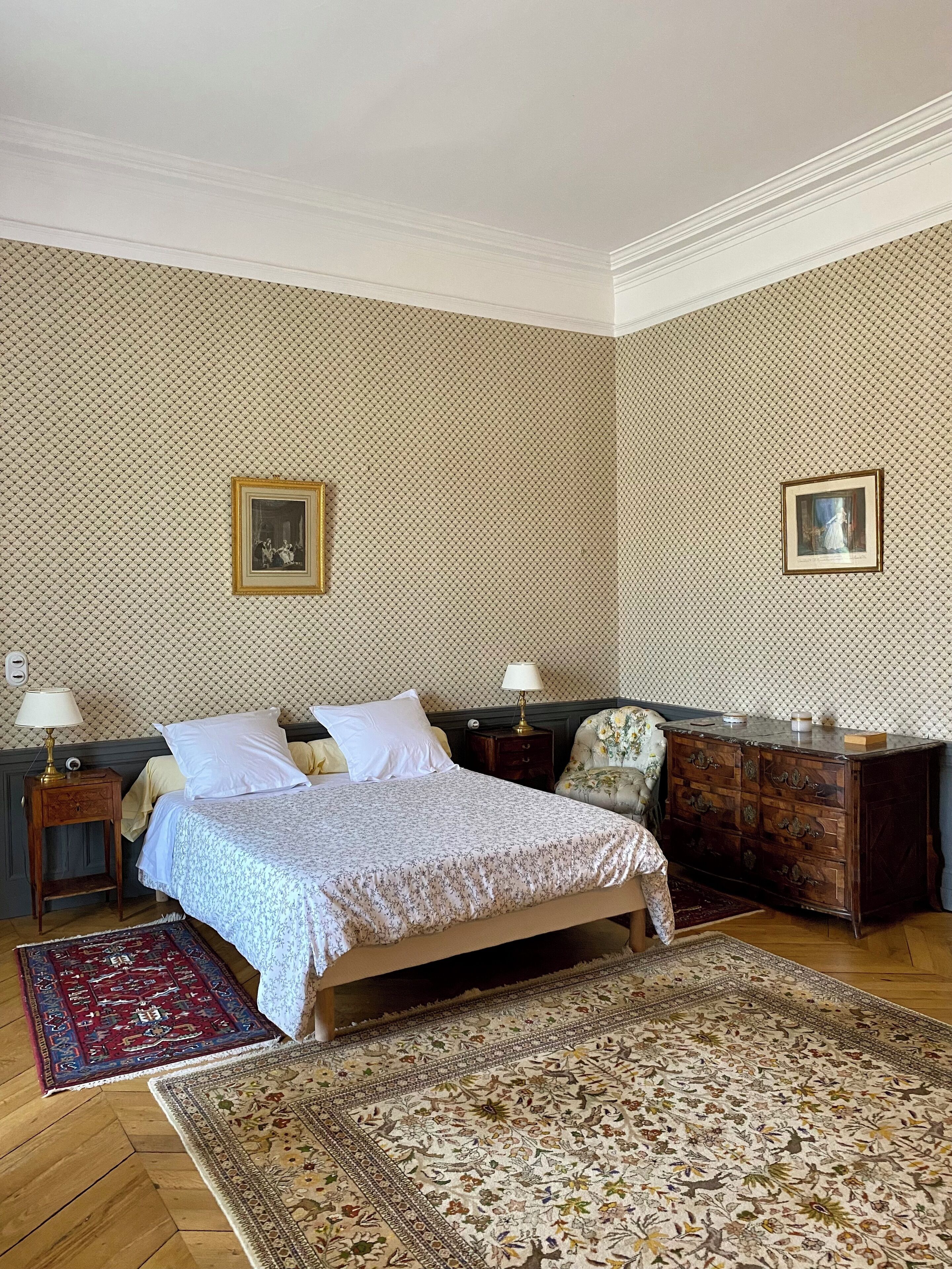 Une chambre à coucher bien rangée, avec un lit, deux tables de chevet, une commode et deux tableaux encadrés accrochés au mur.