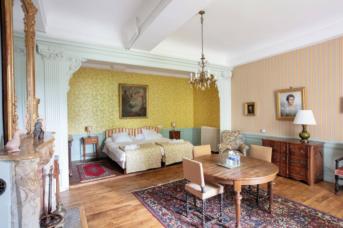 Um quarto com cama, uma mesa de madeira, uma cadeira, cômoda e espelho.