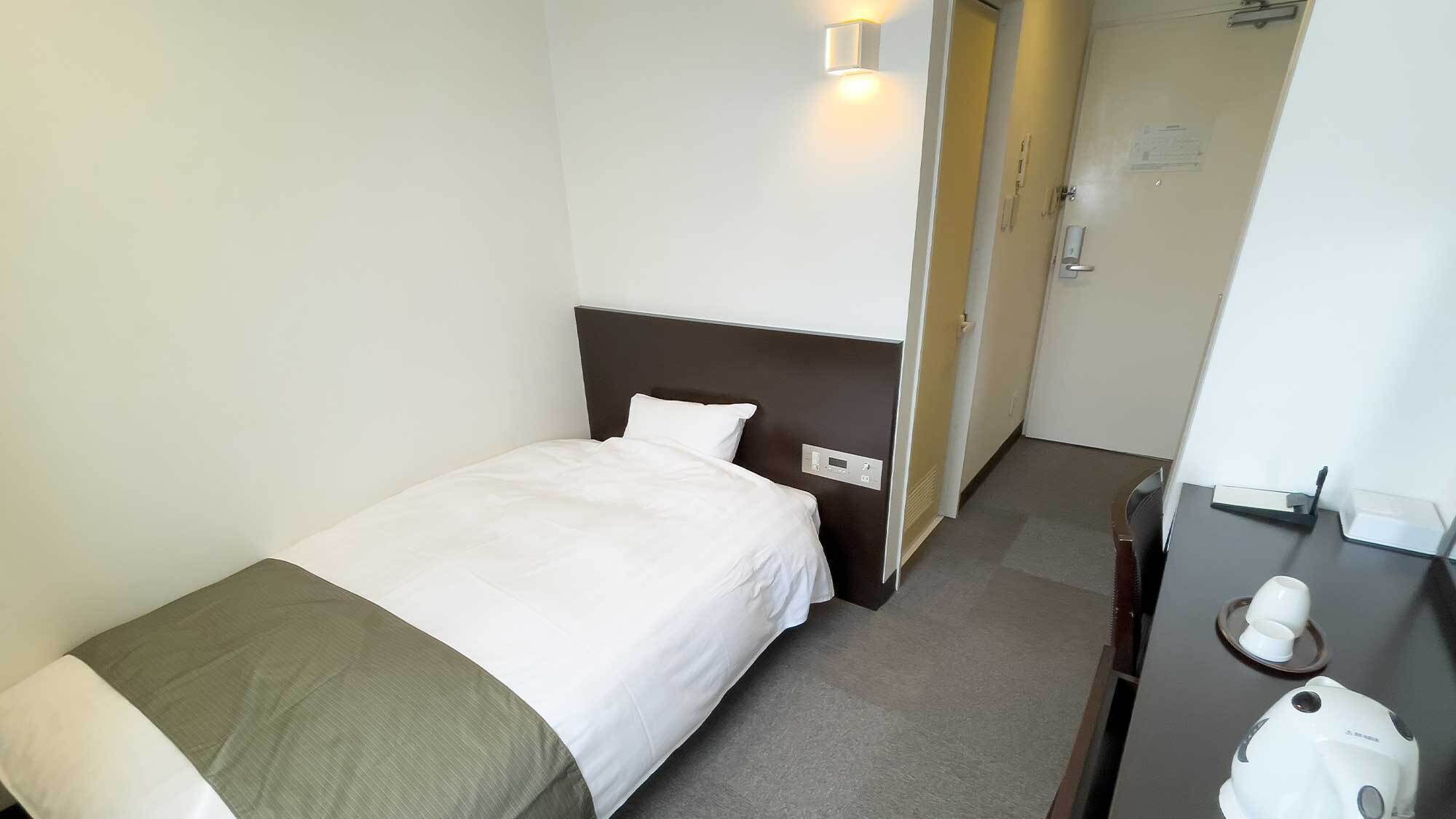 Hotellihuone, jossa on sänky, yöpöytä, peili ja ovi, joka johtaa toiseen huoneeseen.