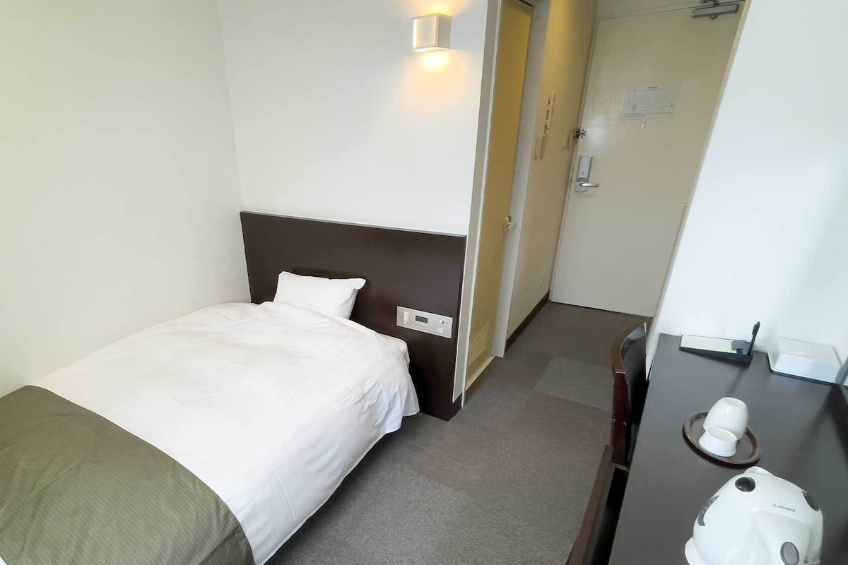 A hotel room with a bed, a bedside table, a mirror, and a door leading to another room.