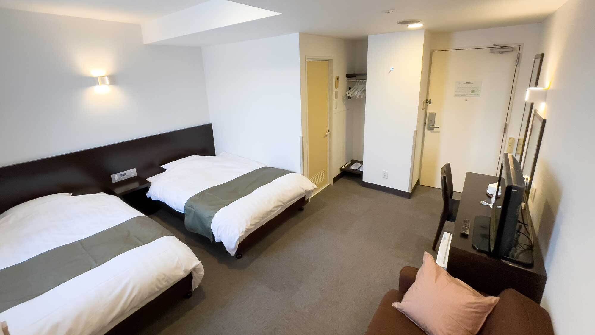 A hotel room with two beds, a TV, a desk, and a mirror.