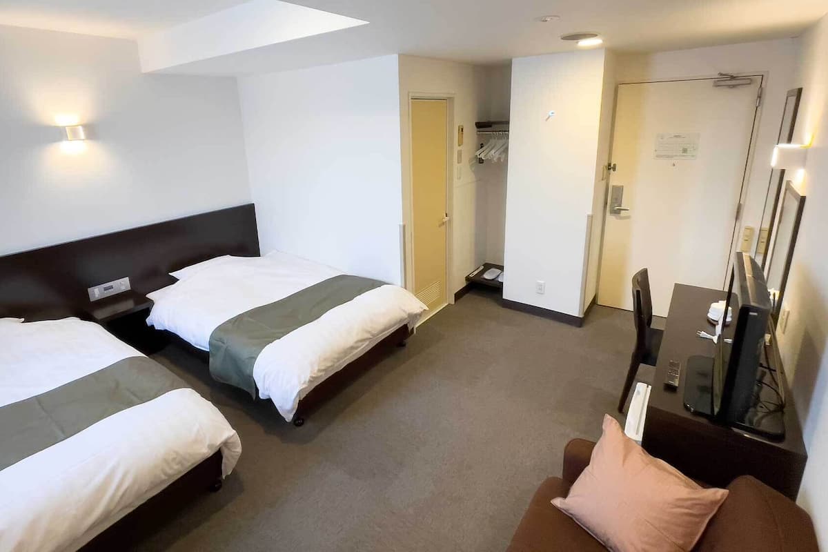 Habitación de hotel con dos camas, televisión, escritorio y espejo.