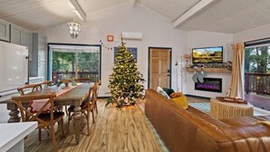 Ein geräumiges Wohnzimmer mit einem Holzespeisetisch, einem Weihnachtsbaum, einem Kamin und einem großen Fenster mit Blick auf Grünflächen.