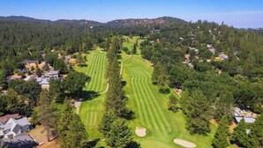 Eine Vogelperspektive eines Golfplatzes mit mehreren Abschlägen und Sandbunkern, umgeben von Wohnhäusern und dichtem Wald.