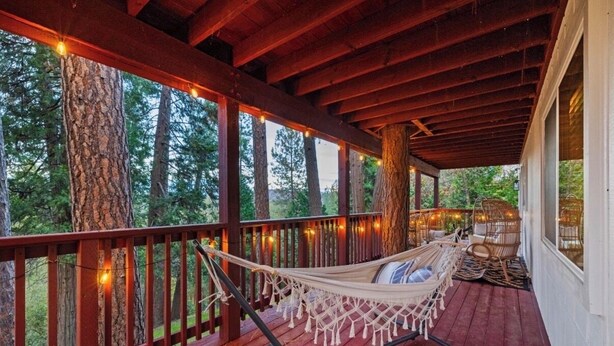 Eine Holzterrasse mit einer Hängematte und Korbstühlen, umgeben von Bäumen und Lichterketten.