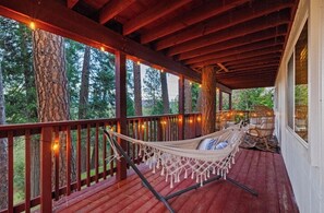 A wooden deck with a hammock and wicker chairs, surrounded by trees and string lights. - Golf, lake, horses, pool, family, friendly in Yosemite—The Black Goose Resort! (Groveland)