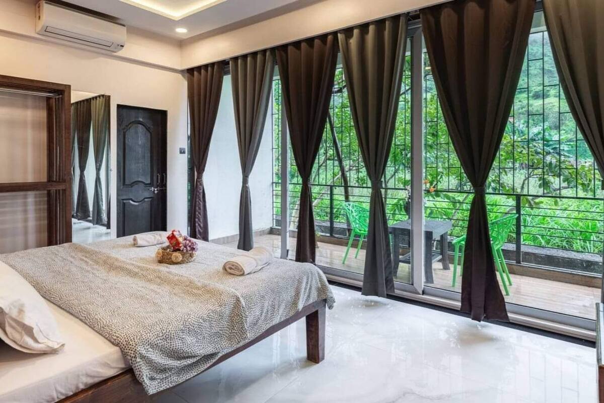 Ein Schlafzimmer mit einem großen Bett, einem Kleiderschrank und Blick auf einen grünen Garten durch große Fenster.