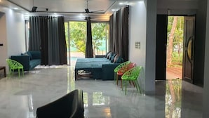 Una habitación de hotel moderna con un conjunto de sofás, una mesa de comedor con sillas y un gran ventanal con cortinas.