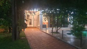Un sendero conduce a un edificio con vestíbulo cubierto, rodeado de follaje y árboles.