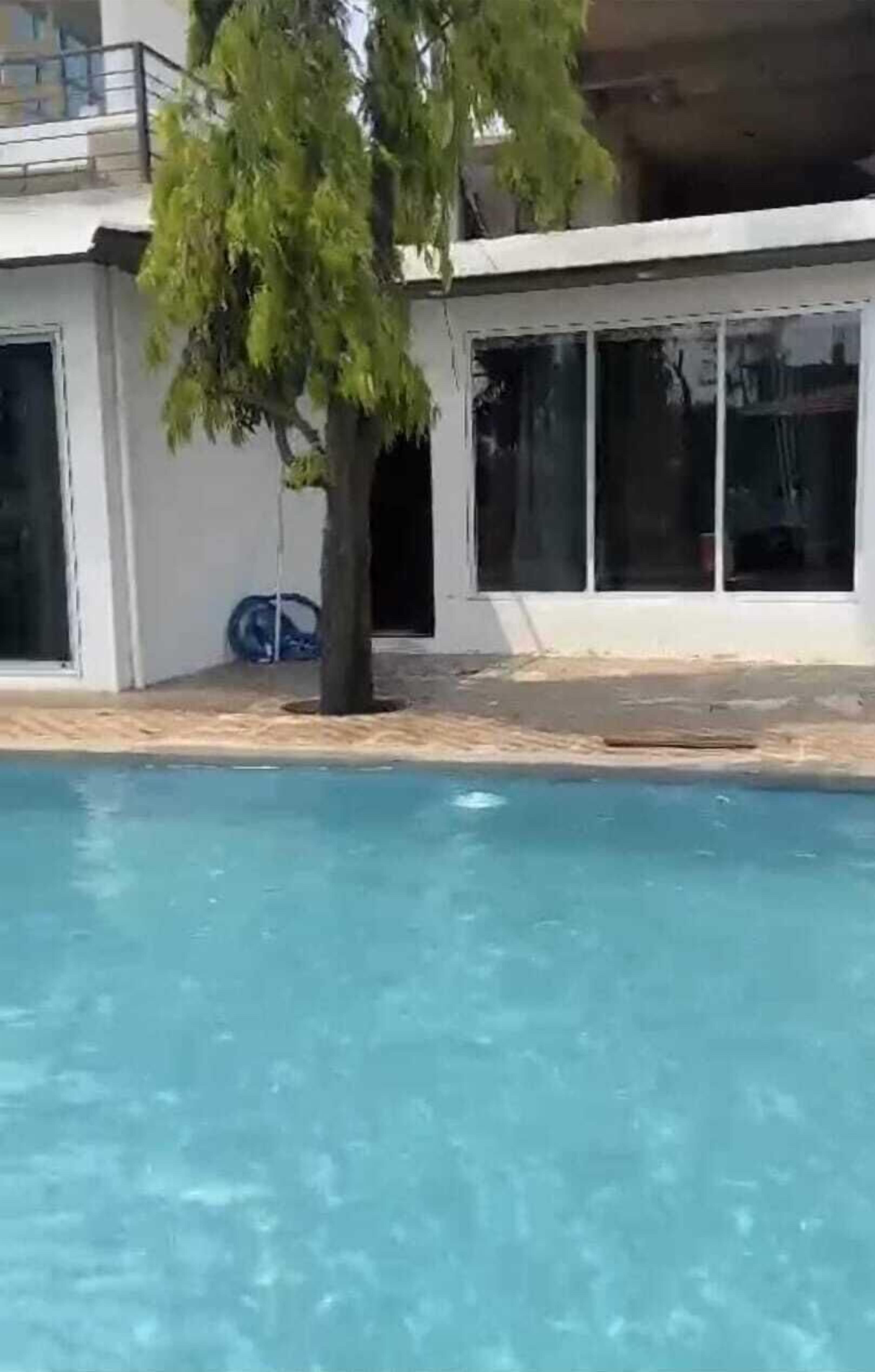 Ein Schwimmbecken im Vordergrund, im Hintergrund ein Gebäude mit großen Fenstern und ein klarer Himmel.