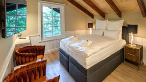 Een slaapkamer met een groot bed, twee bedlampjes, een raam met uitzicht op bomen en een houten plafond.