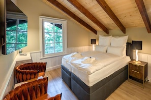 Ein Schlafzimmer mit einem großen Bett, zwei Nachttischlampen, einem Fenster mit Blick auf Bäume und einer Holzbalkendecke.