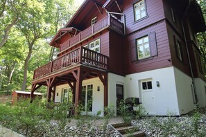 Ein zweistöckiges Holzhaus mit Balkon, umgeben von Bäumen.