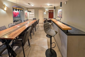 Un comedor moderno con una larga mesa de madera, varias sillas, una barra y luces colgantes.