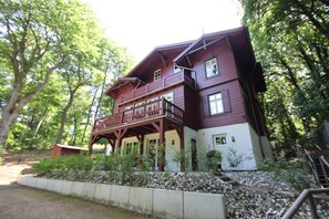 A two-story wooden building with a balcony, surrounded by trees.