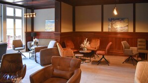 Een hotel lobby met lederen fauteuils, een houten receptiebalie en kunstwerken aan de muur.