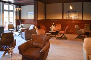 A hotel lobby with leather chairs, a wooden reception desk, and artwork on the walls.