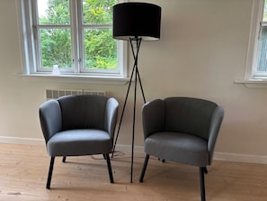 Två grå fåtöljer, en svart golvlampa och ett fönster med utsikt över träd.