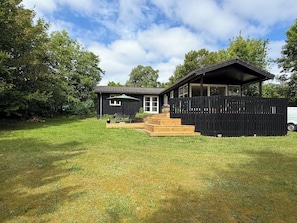 Une maison moderne dotée d’une terrasse, d’une cour clôturée et d’un fourgon blanc garé à proximité.