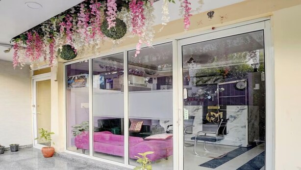 A hotel entrance with a glass door, a pink sofa inside, and a reception desk with a sign. - Hotel MoonLit (Noida)