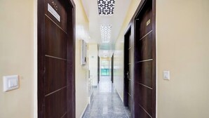 A hallway with marble flooring, dark wooden doors, and a ceiling with a geometric pattern. - Hotel MoonLit (Noida)